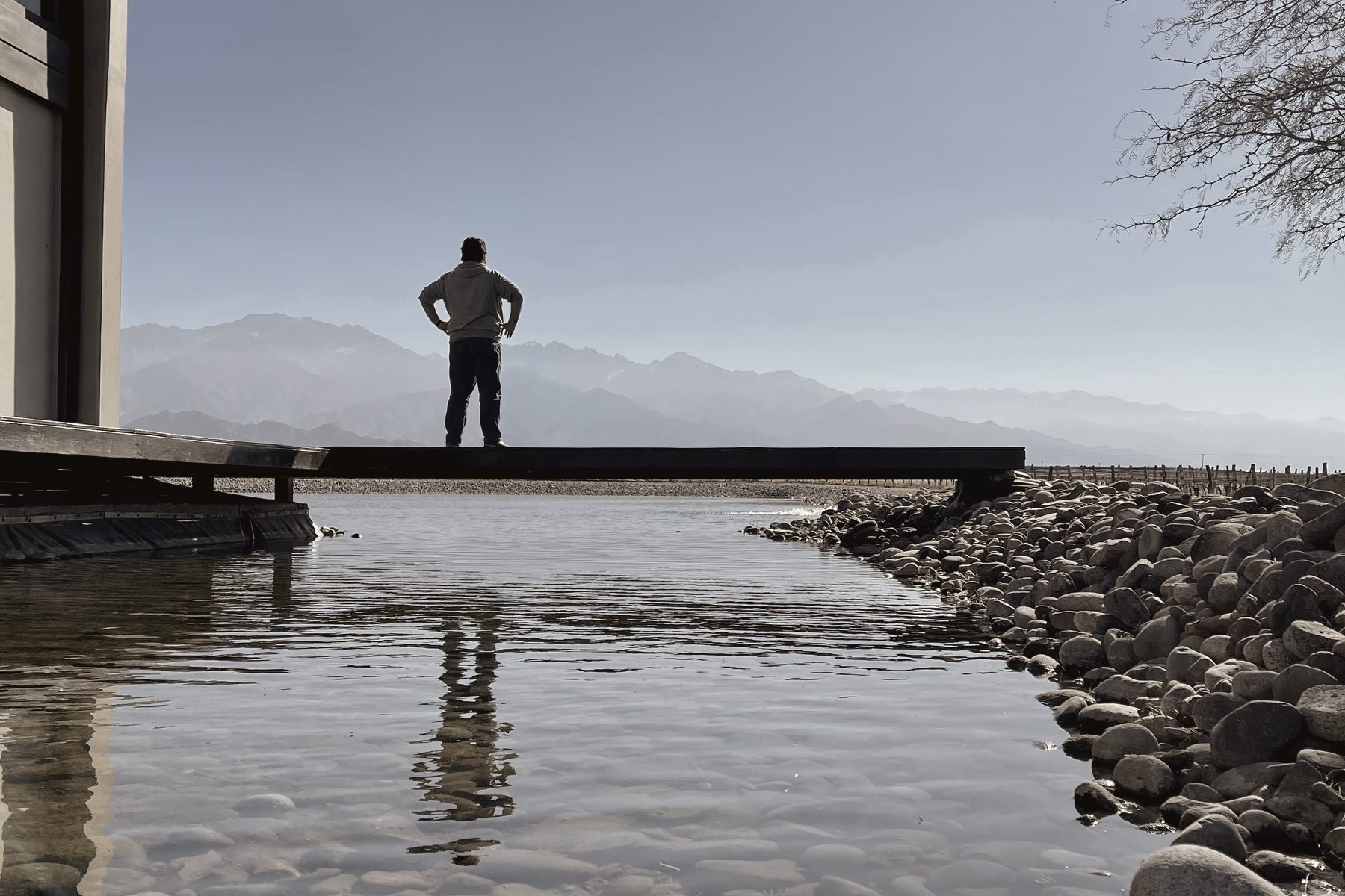Lucas Wall at the end of a pier, looking out over still water toward the Andes.
